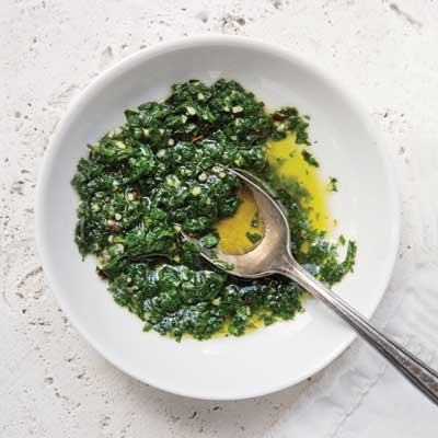 a bowl of green chimichurri with a spoon in it