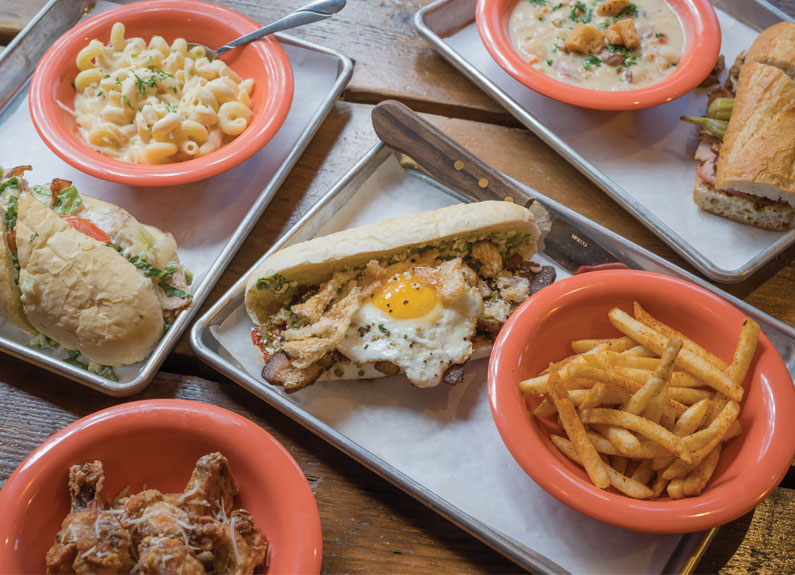 several sandwiches and sides on metal trays on a table