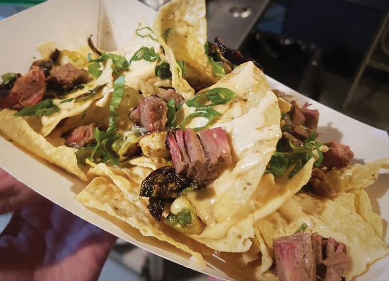 a paper basket with nacho chips covered in brisket and cheese