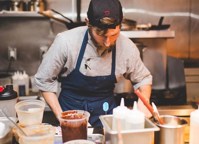 a chef with a baseball cap and blue apron working with food