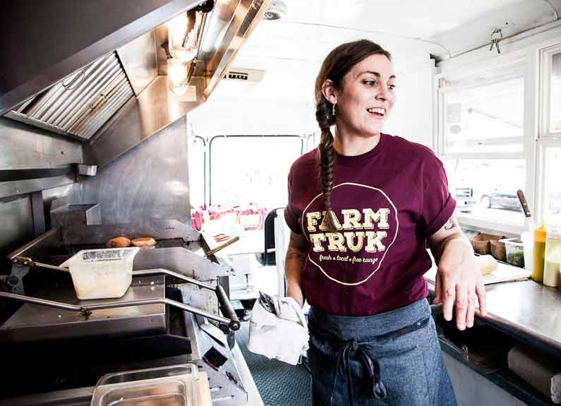 a woman in a farmtruk tshirt cooking inside a food truck