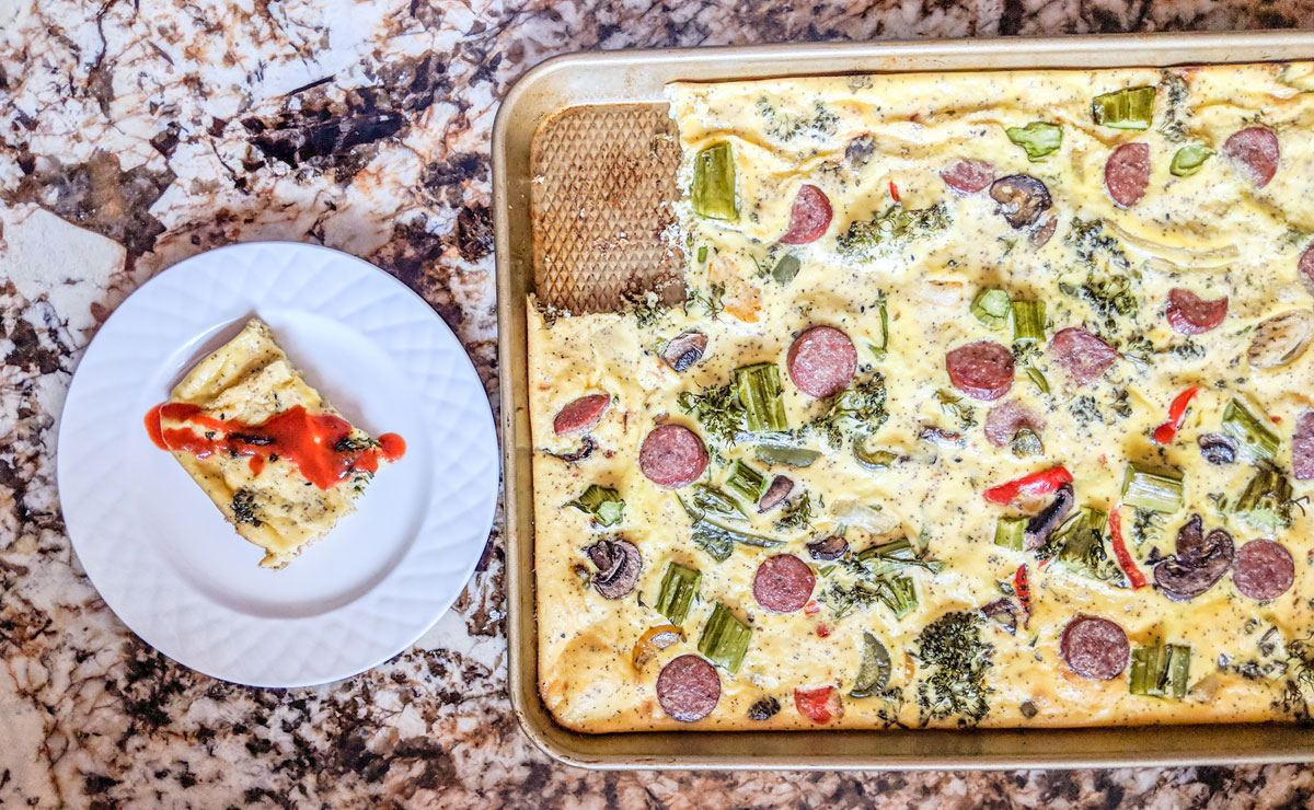 a sheet pan filled with an omelet next to a dish with a slice of omelet with sriracha