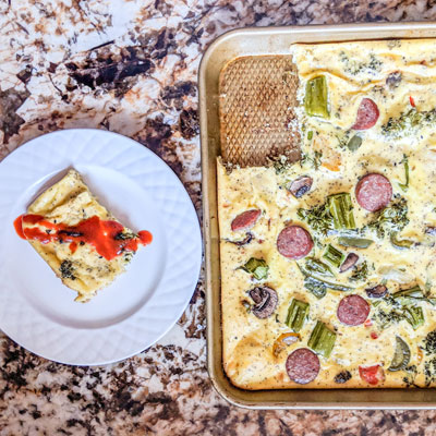 a sheet pan filled with an omelet next to a dish with a slice of omelet with sriracha