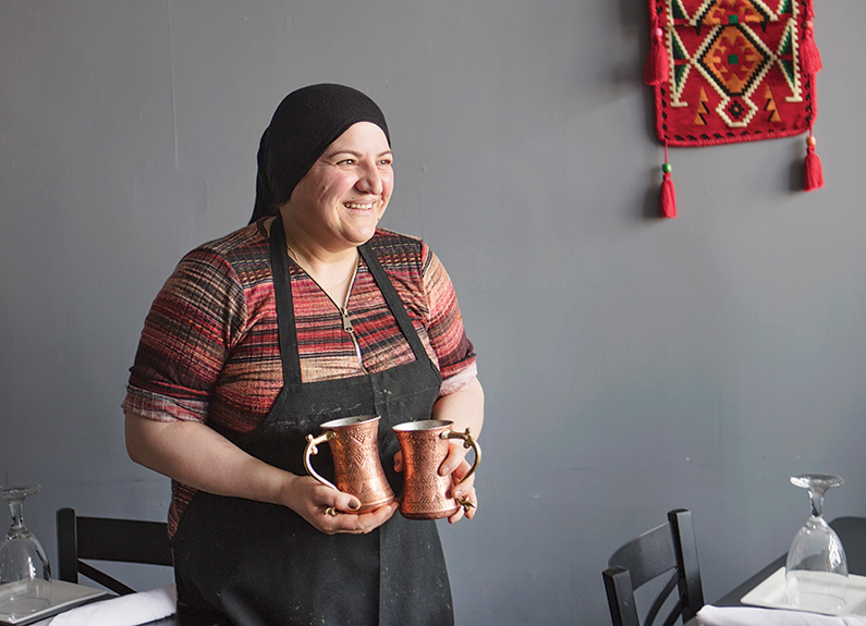 a woman in a black apron holding copper pitchers 