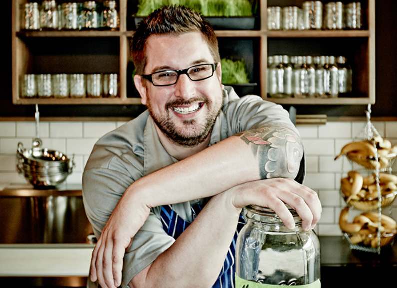 a smiling man with glasses leaning on a jar