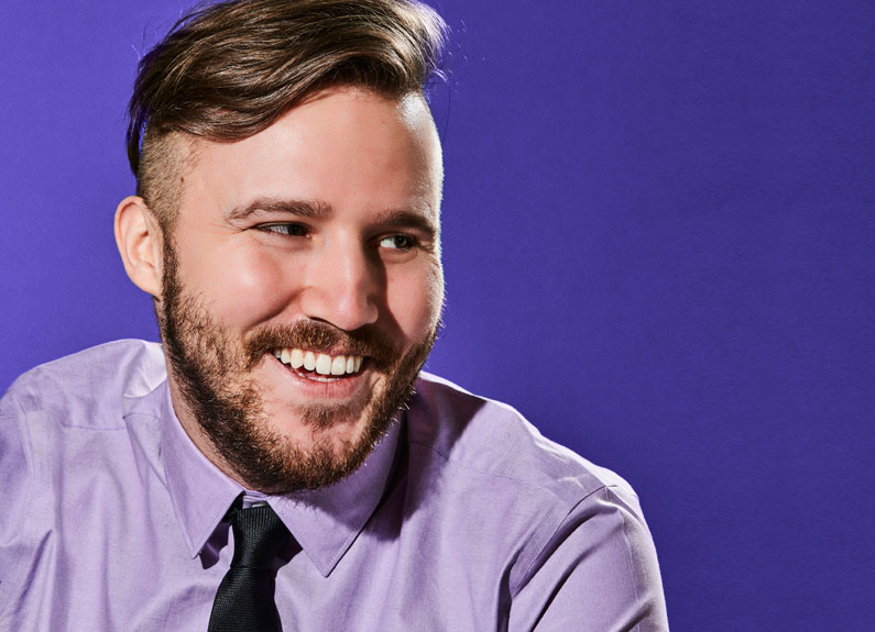 a smiling man against a purple backdrop