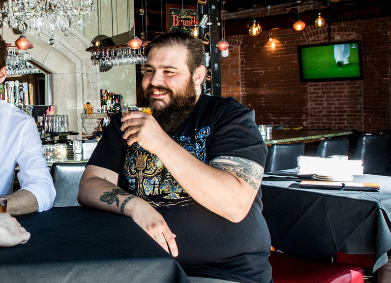 a smiling man drinking a cocktail at a bar