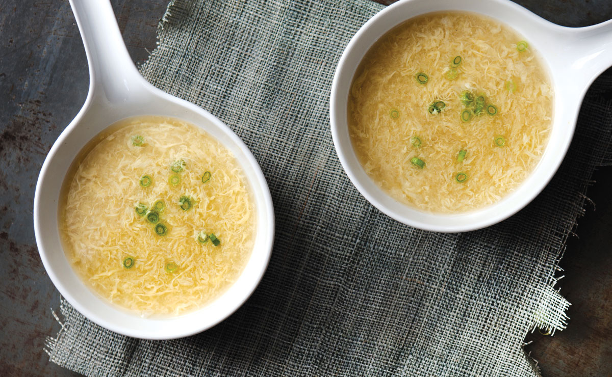 two white bowls with handles filled with egg drop soup