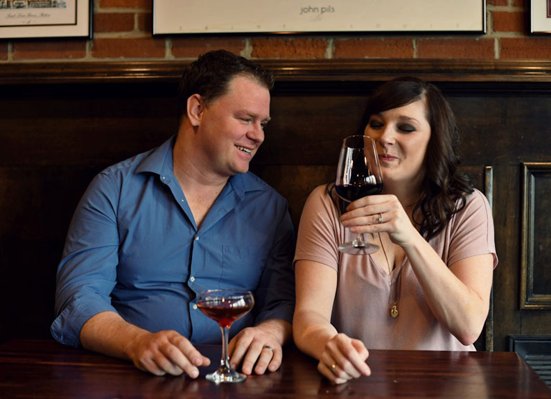 a couple sitting at a booth with glasses of red wine