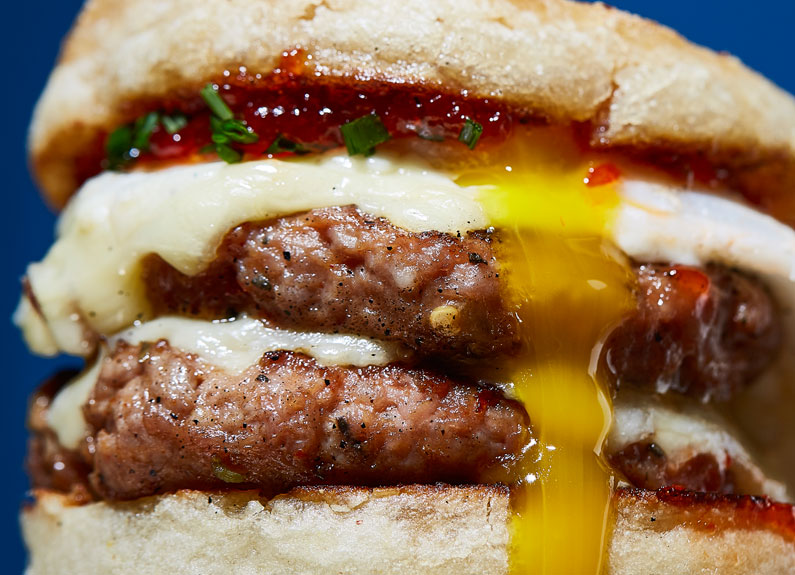 a close-up photo of double sausage patty breakfast sandwich with cheese and egg