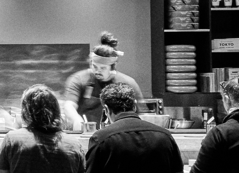 a sushi chef in action at a busy sushi bar