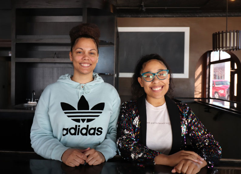 two young women smiling at the camera behind a counter