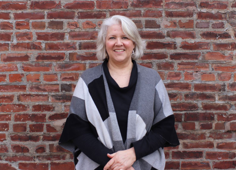 a smiling woman in a gray and black wrap in front of a brick wall