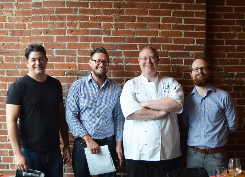 four smiling men standing in a restaurant dining room 