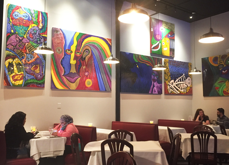 a dining room with white tablecloths and bright artwork