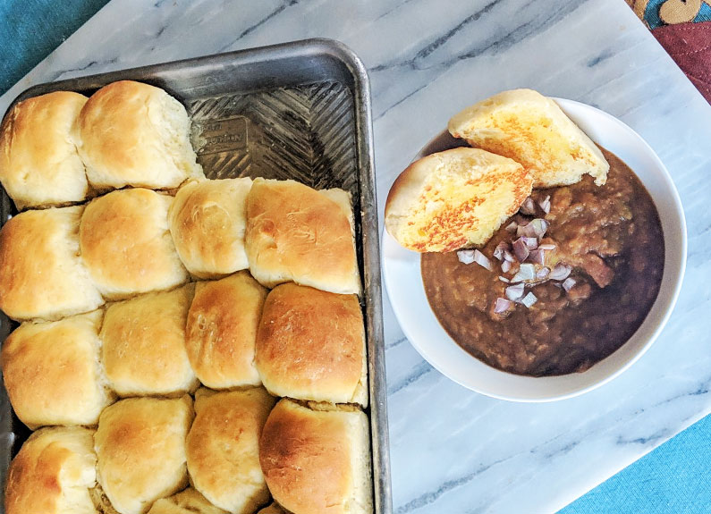 a bowl of indian curry with a tray of dinner rolls