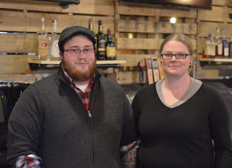 a man with a flat cap and a blonde woman in front of a bar