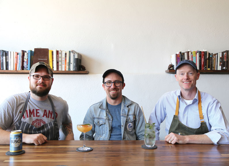 three men sitting at a bar with cocktails