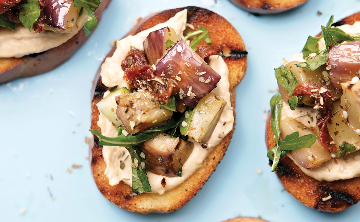 a plate of crostini topped with hummus and eggplant