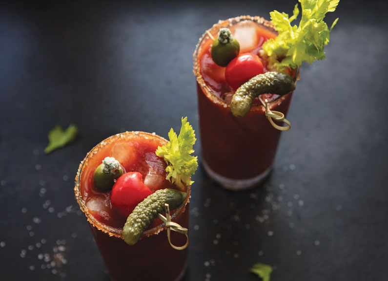 two bloody marys with pickles, tomatoes and salt rims for garnish