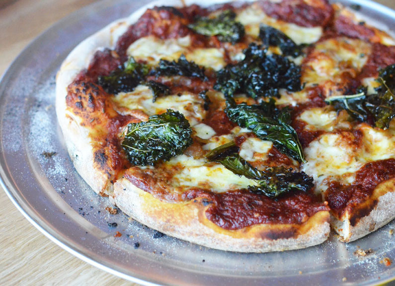 a pizza on a silver pizza pan with basil