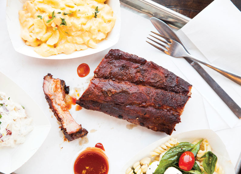 three barbecue ribs with sides of mac and cheese and salad on a white tablecloth