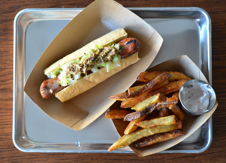 a sausage in a paper basket and fries and a dip in paper basket