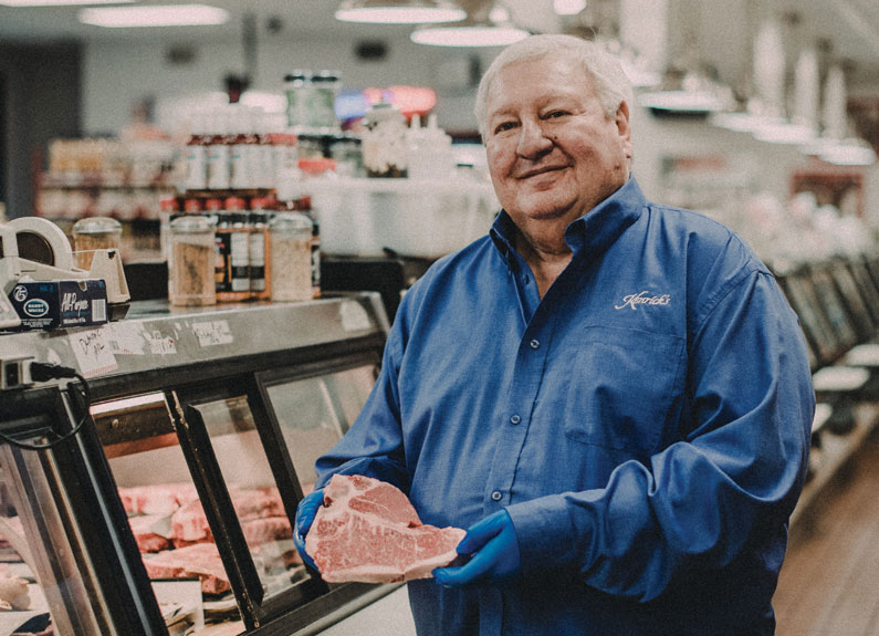 a man with gray hair and a blue shirt holding a raw steak next to a butcher counter