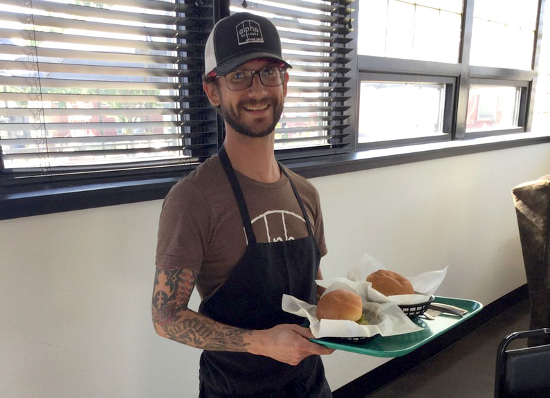 a man in a black apron and baseball cap holding a tray of fod