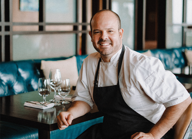 a black and white photo of a smiling man in a chef coat