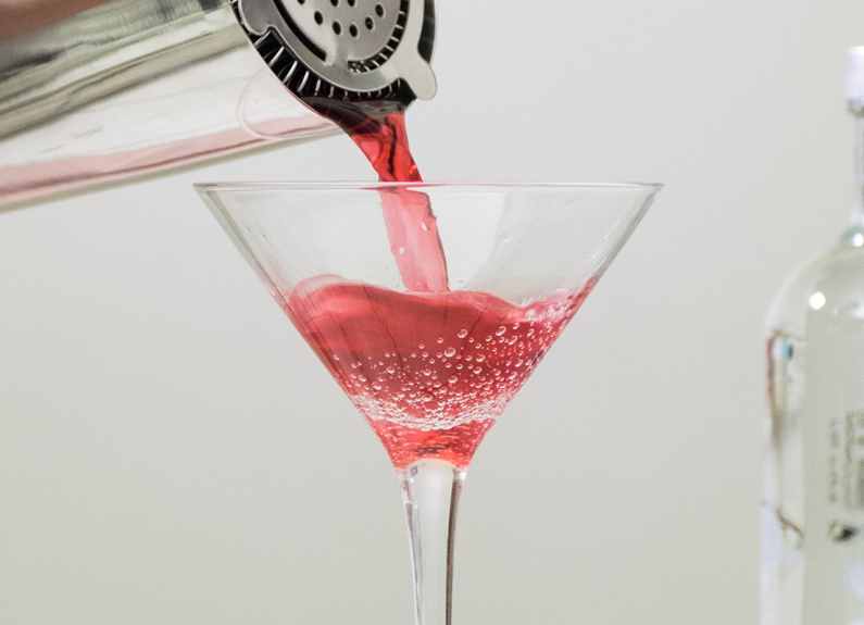  a cocktail shaker pouring a pink drink into a martini glass