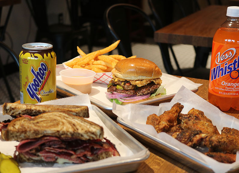 burgers, sandwiches and chicken wings on metal trays with sodas