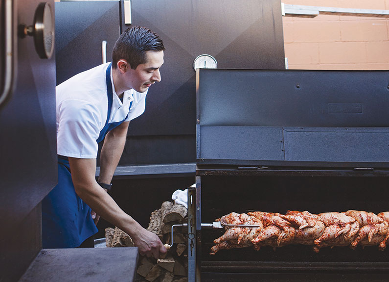 andrew enrique cisneros works on his brasas de pollo, a peruvian rotisserie-style chicken