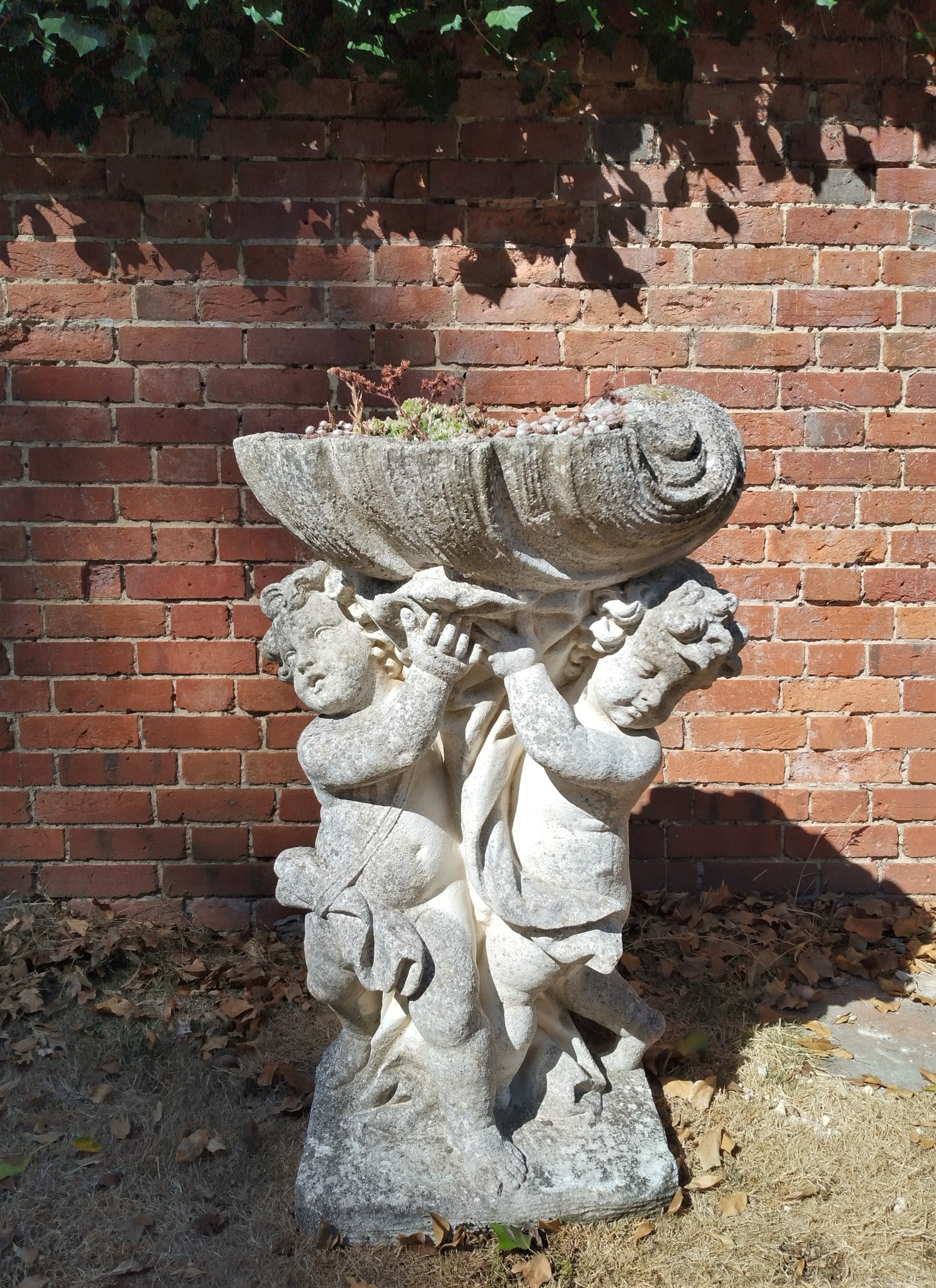 A composition stone figure of two cherubs holding a shell bowl