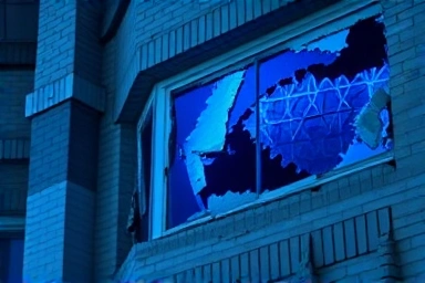 손상된 건물의 클로즈업으로, 갈라진 벽과 부서진 창문을 상세히 보여주며, 스타일은 포렌식 사진과 유사하고, 차가운 푸른색 조명과 세밀한 디테일로 사고의 심각성을 강조합니다.