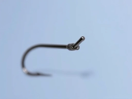 A close-up, sharp image focusing on the barb and point of a specific fishing hook, highlighting its sharpness and design for different fish species.