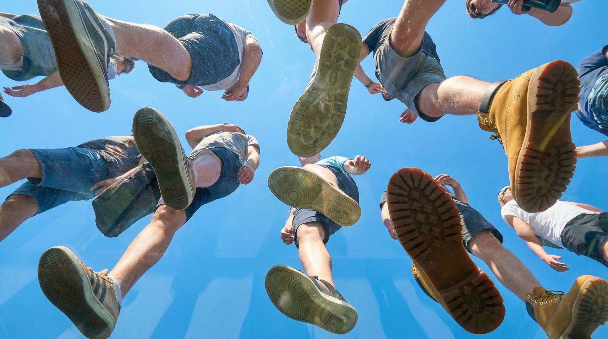 Underfoot Perspective: People Walking on Transparent Plexiglass Against Blue Sky - Example 1