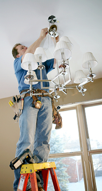 Master Electrician changing light fixture while standing on a ladder