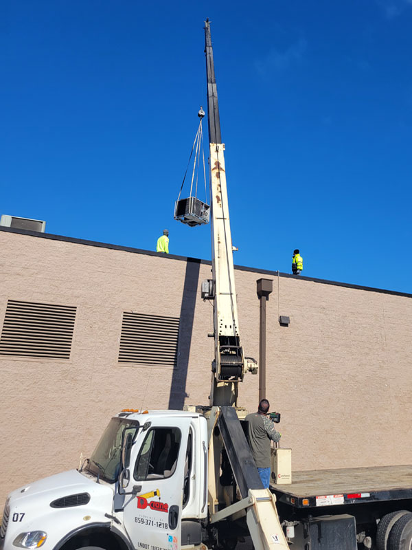 Crane lifting off old rooftop HVAC unit while new Carrier RTU unit is on deck to be placed upon new curb on rooftop