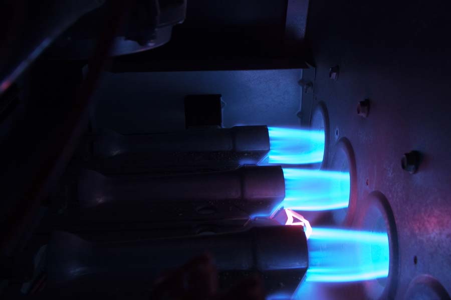 gas burners with bright blue flames inside an operating gas furnace