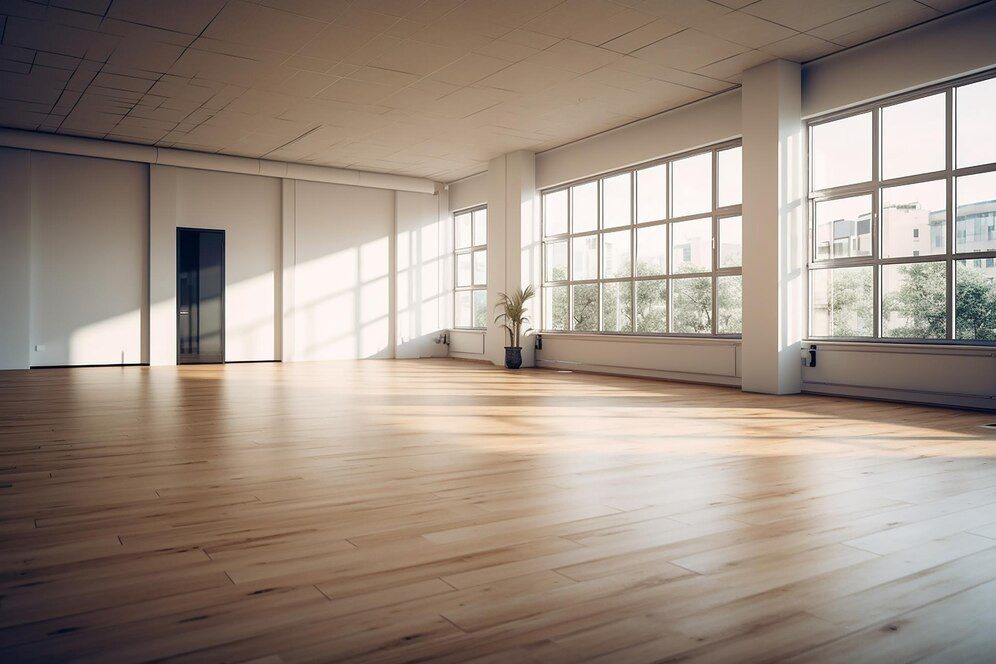 A room with a wooden floor, and sunlight come in through the windows.