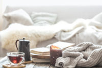 Still-life home comfort in the living room with a cup of tea, a lit candle, and a knitted sweater.