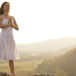 Woman meditating on hillside embraces gratitude as a spiritual practice.