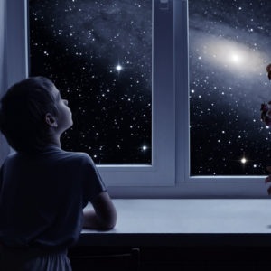 A little boy is standing near the window and looking outside at stars