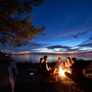 Group of people around campfire under evening sky.