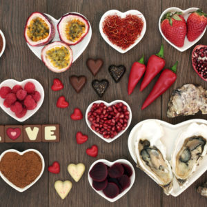 Aphrodisiac foods in heart-shaped bowls and loose on oak wood background
