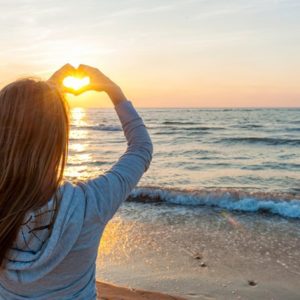 Girl with heart hand sign at sunset