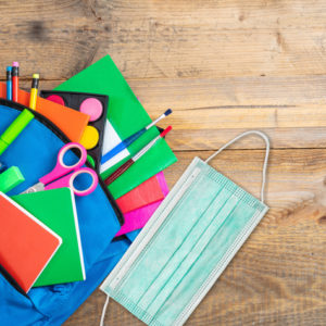 Back to school in time of coronavirus. School supplies and medical protective face mask with backpack.