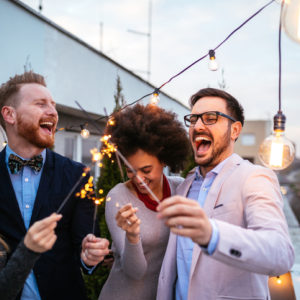 Multiracial and multi gender group of four friends at a rooftop party hold sparklers