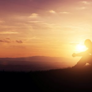 Man on hill at sunset practicing spiritual affirmations